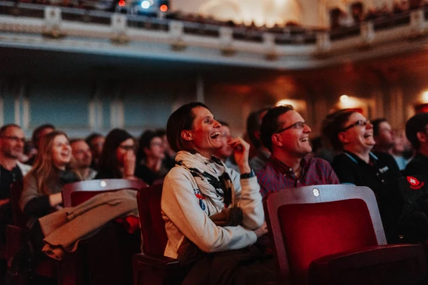 Smiling audience in an event hall, engaged in an entertaining film event.