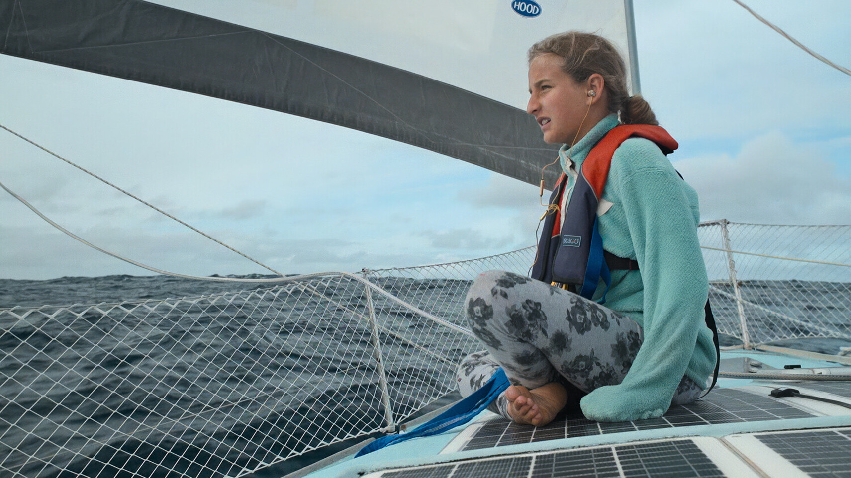 Salina Schw&ouml;rer sitting on the deck of the TOPtoTOP expedition catamaran with a life jacket, barefoot, gazing at the ocean horizon during an offshore sailing passage